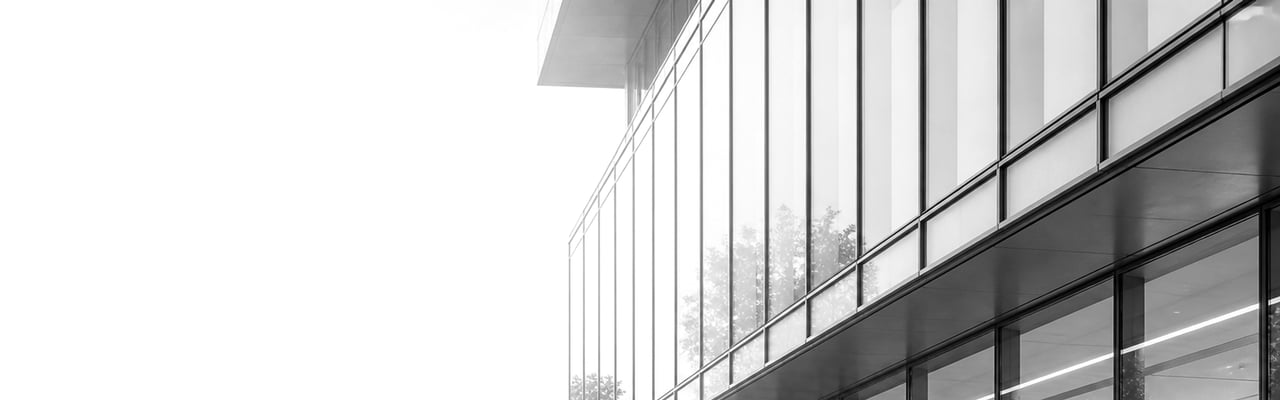 A calm view of a contemporary glass-fronted office entrance with soft daylight reflecting off the facade.