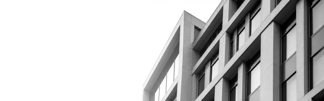 A modern monochrome corporate building with repeating window grids and sharp geometric shadows, photographed against a near-white sky.